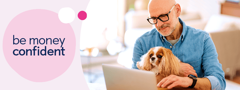 Man holding a black and white cat whilst using a laptop