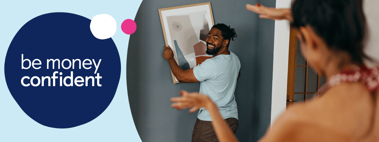 Couple hanging up a frame containing artwork