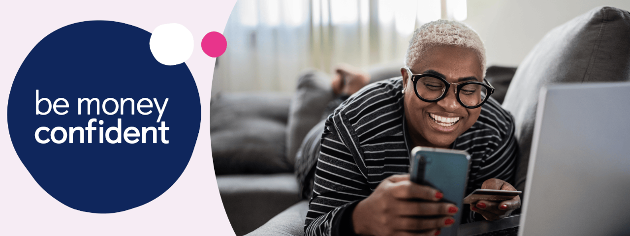 Person laying on a sofa whilst using a mobile phone and holding a bank card