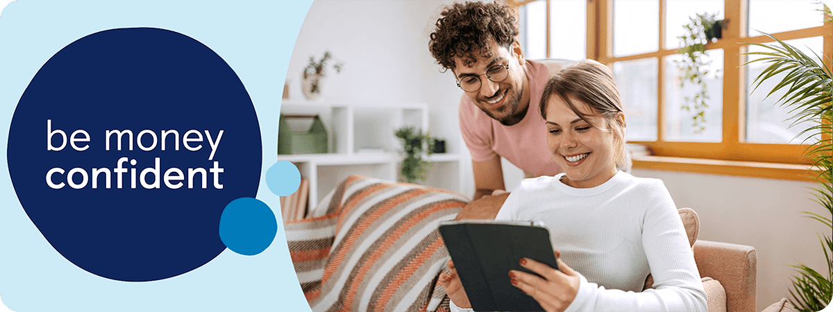 Person sat on sofa looking at tablet with person stood behind them