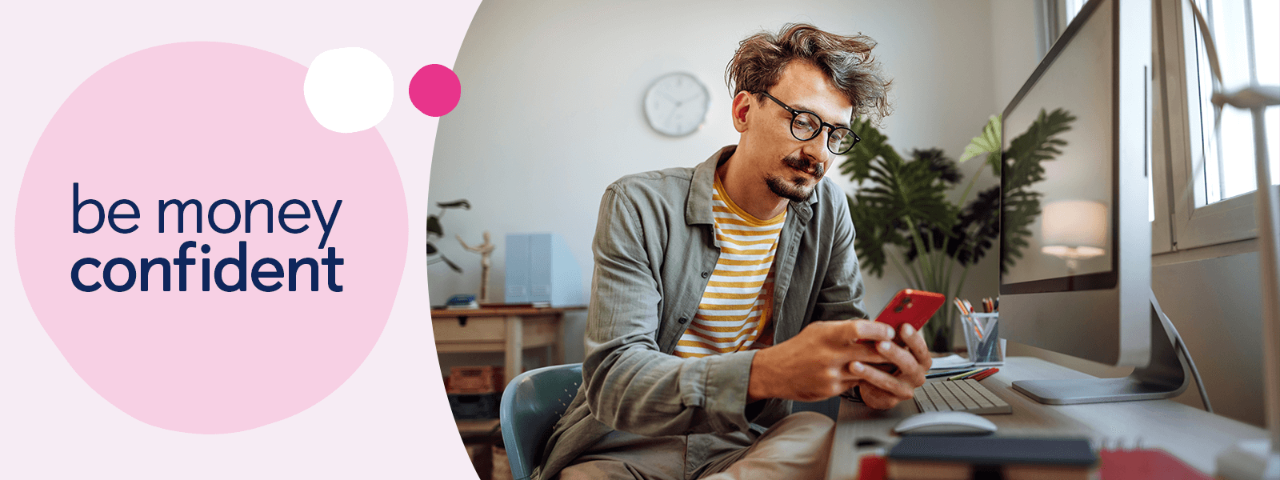 Person sat at computer desk looking at mobile phone